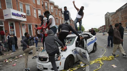 Demonstrators in Baltimor climb on a destroyed police car on April 27, 2915.