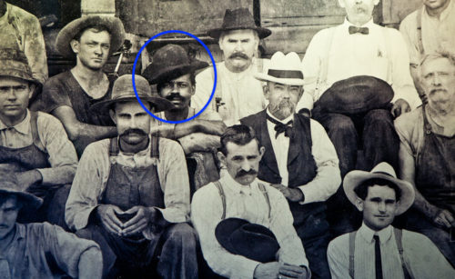 A man believed to be the son of Nearis Green sits at the right hand of Jack Daniel (center, in white hat). This photo, in Daniel’s old office,was taken at his distillery in Tennessee in the late 1800s. 