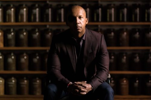 Bryan Stevenson sits in front of a wall of jars filled with soil collected from lynching sites across the country. Credit: Nick Frontiero, HBO 