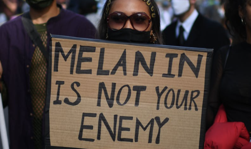 Woman holding sign "Melanin Is Not Your Enemy"