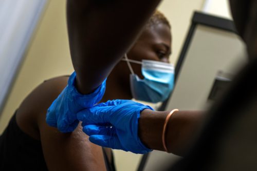 A person of color getting vaccinated while wearing a face mask.