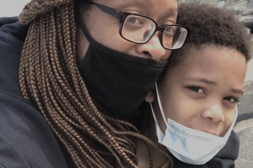 A black woman holding her child while wearing masks.