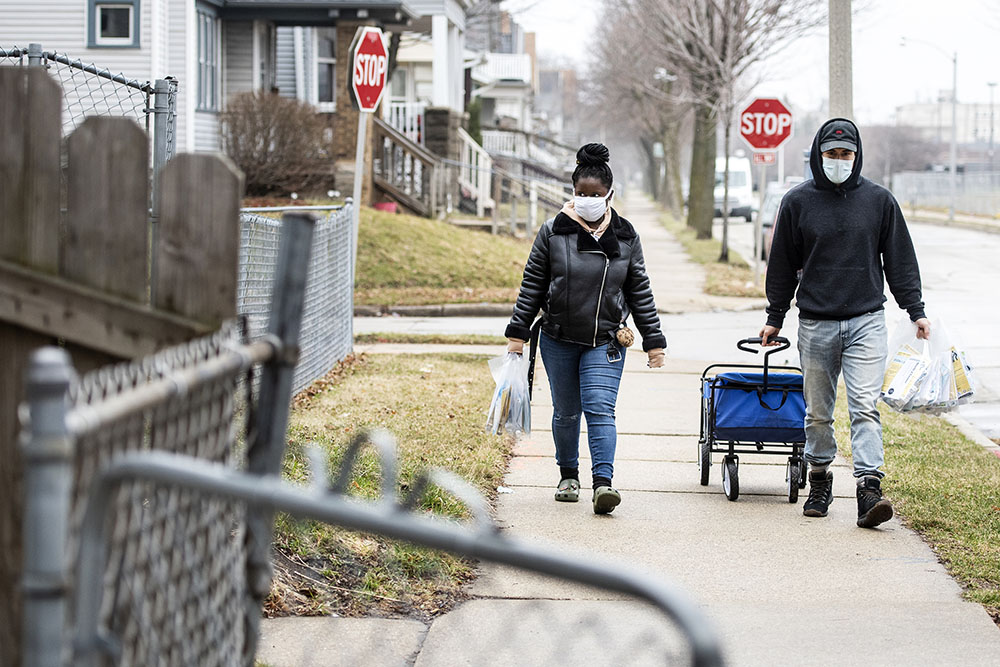 Kynala Phillips, left, and Jimmy Gutierrez, right, distribute bags with COVID-19 vaccination information, face masks, hand sanitizer and a community newsletter to Milwaukee residents in vaccine eligible ZIP codes on March 27, 2021, in Milwaukee. Some of Wisconsin’s most vulnerable populations struggle to access COVID-19 vaccines, and volunteers and community groups are trying to erase barriers. (Angela Major/WPR)
