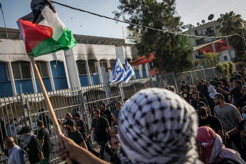 Palestinians gesture and wave Palestinian flags at Israelis in a Jewish community building, during renewed riots in the city of Lod on May 11.