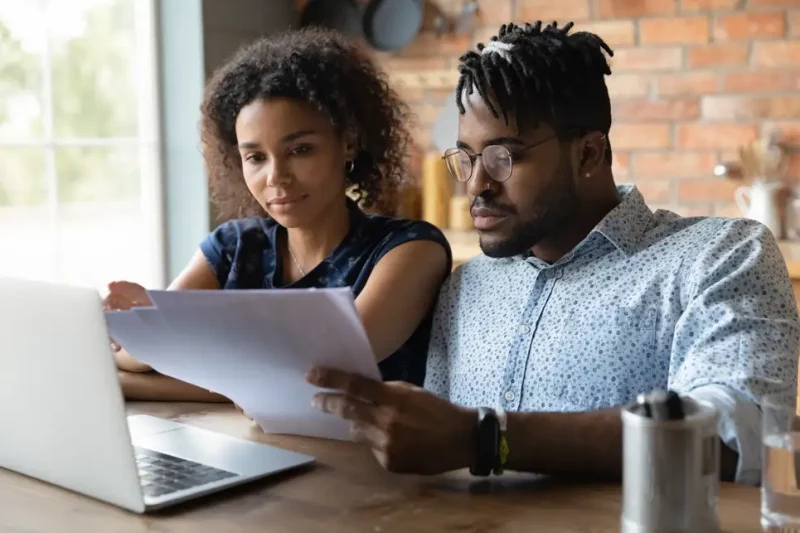 A Black couple looking at paperwork and a laptop