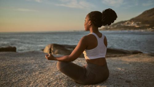 A black woman meditates on the beach (Getty)