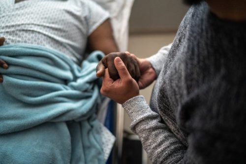 A black patient holds a visitor's hand