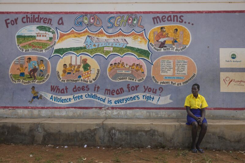 A Ugandan boy sitting in front of a mural